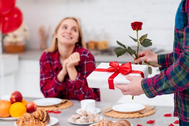 Close-up man surprising woman with rose and gift