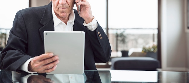 Close-up of a man talking on mobile phone looking at digital tablet in the office