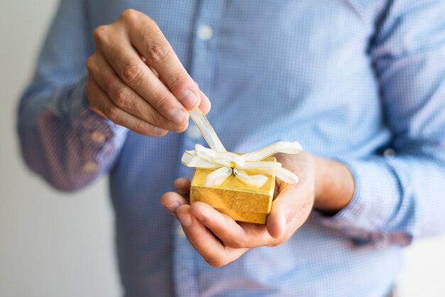 Close-up of man untying bow on small yellow box