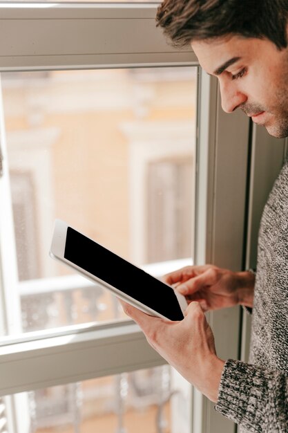 Close-up man using tablet near window