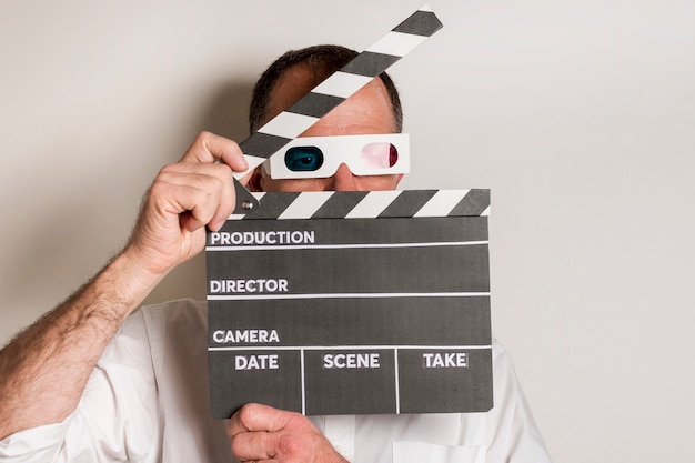 Close-up of a man wearing 3d glasses holding clapperboard against white backdrop