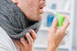 Free photo close-up of a man wearing gray scarf around his neck using a spray to treat sore throat