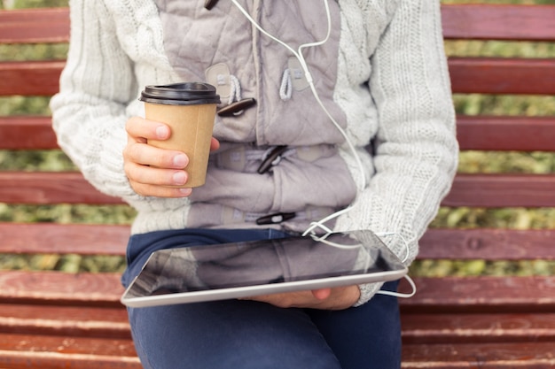 Close up of man with tablet computer reading news at autumn motning with paper cup of coffee