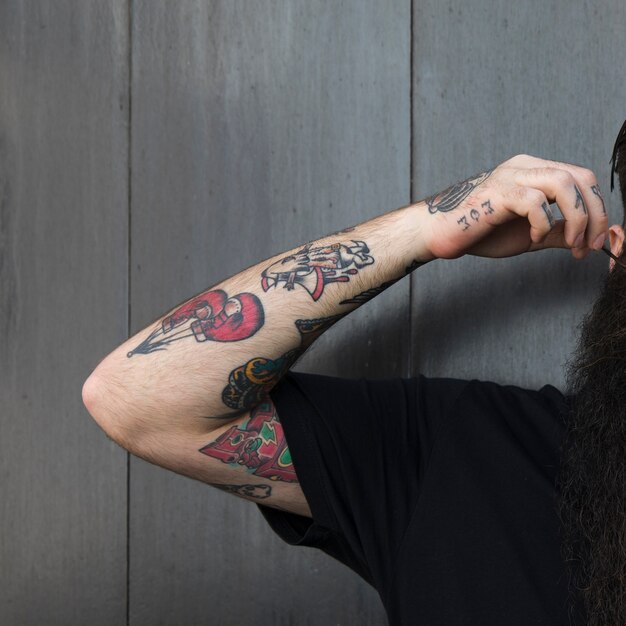 Close-up of a man with tattoo on his hand standing against grey wooden wall