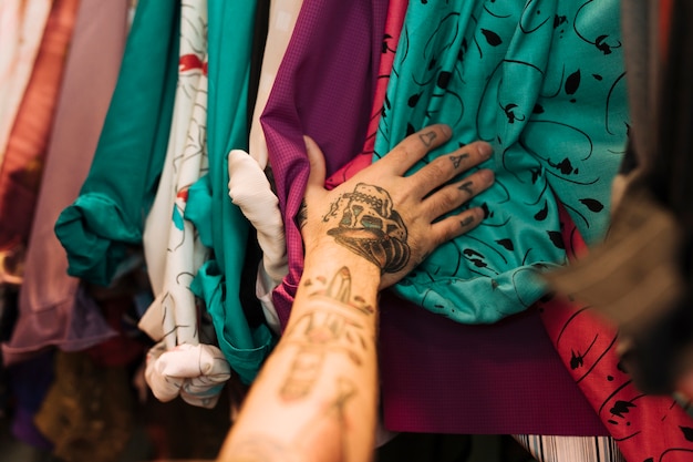 Close-up of a man with tattoo on his hand touching shirts arranged on the rail