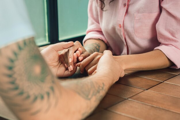 Close up on a man and a woman holding hands at a wooden table