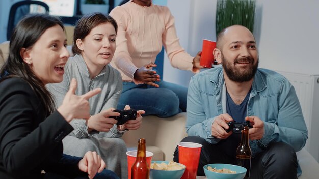 Close up of man and woman using controllers to play video games on tv console to do fun activity after work. Colleagues enjoying game on television and drinks at office after hours.