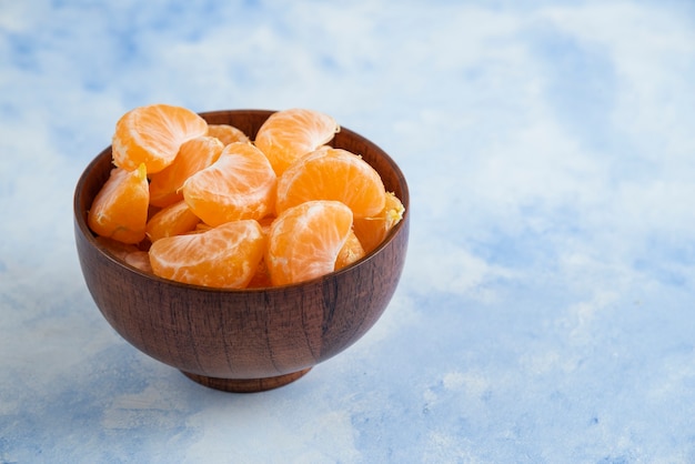 Close up of Mandarin slices in wooden bowl on blue surface