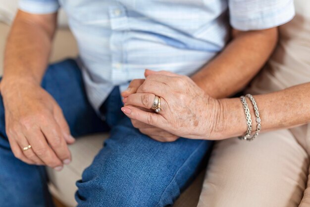 Close up of mature old husband and wife hold hands show love and care Senior couple holding hands while sitting together at home Elderly relationships marriage concept