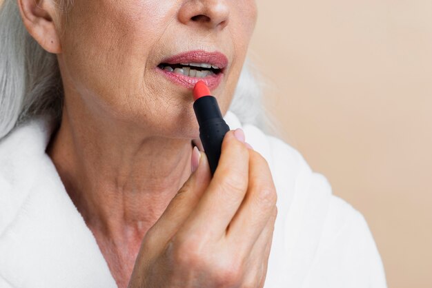 Close-up mature woman applying lipstick
