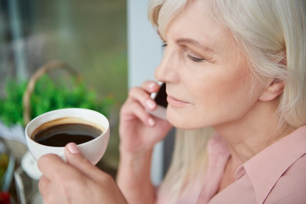 バルコニーでおいしいコーヒーを楽しんでいる成熟した女性にクローズアップ