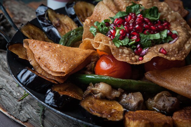 Close-up meat with baked potatoes, eggplant, tomato, pepper and decorated with pomegranate on wooden bark