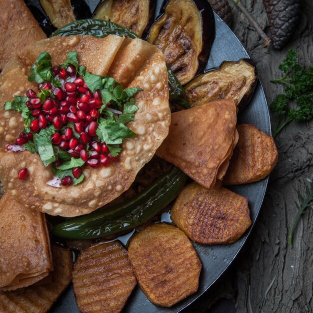 Close-up meat with baked potatoes, eggplant, tomato, pepper and decorated with pomegranate on wooden bark