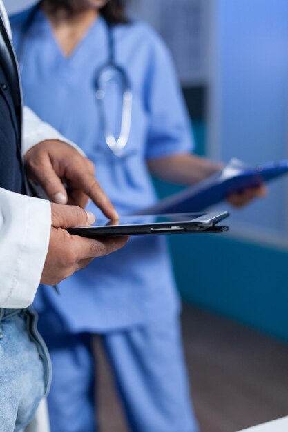 Close up of medic pointing at tablet screen for medical practice, working late. Doctor using modern device with touch screen and talking to assistant about healthcare system overtime.