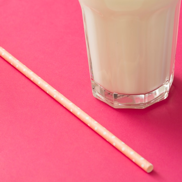 Close-up of milk glass with drinking straw on pink backdrop