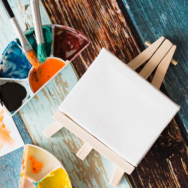 Close-up of minimal white blank easel with paint palette and paintbrush on wooden surface