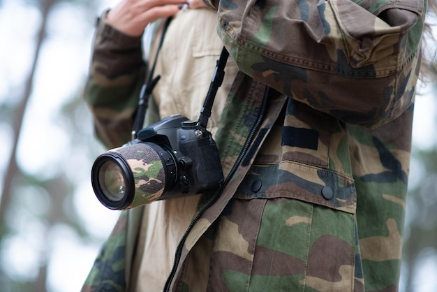 Close-up of modern black camera. Digital camera with big lens on lace against coat in military style. Technology, hobby concept