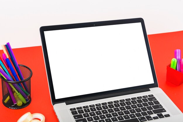 Close-up of modern laptop with blank white screen on red table