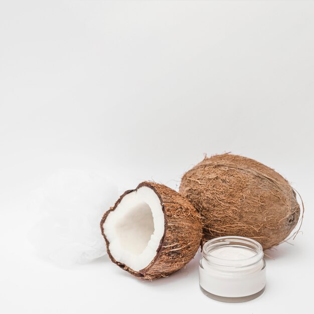 Close-up of moisturizing cream; loofah and coconut on white backdrop