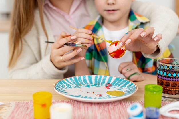 Close-up mom helping son to paint eggs