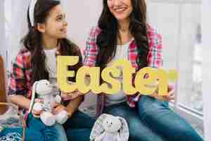 Free photo close-up of mother and daughter holding bunny and easter word in hand