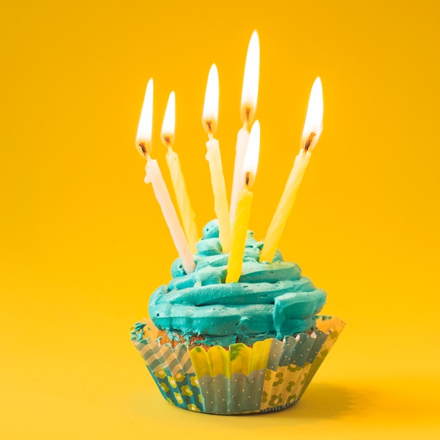 Close-up of muffin with burning candles on yellow background