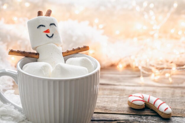 Close up mug of hot drink with marshmallow snowman on blurred background