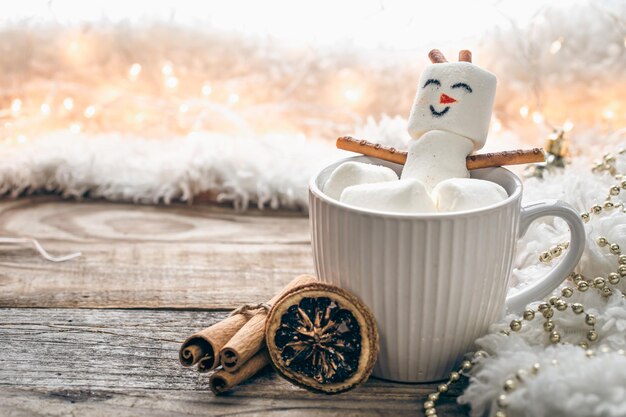 背景をぼかした写真にマシュマロ雪だるまと温かい飲み物のマグカップを閉じる