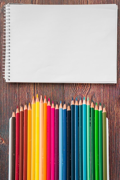 Close-up of multicolored pencil and white spiral note book on wooden desk