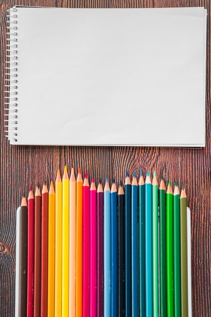 나무 책상에 여러 가지 빛깔 연필과 흰색 나선형 참고도 서의 근접