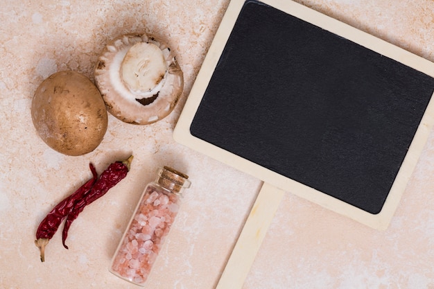 Free photo close-up of mushroom; chili peppers and himalayan salt bottle near the blank wooden placard