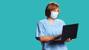 Free photo close up of nurse chatting with patient on laptop during online telehealth checkup appointment. happy healthcare expert isolated over studio background using gadget, wearing medical face mask