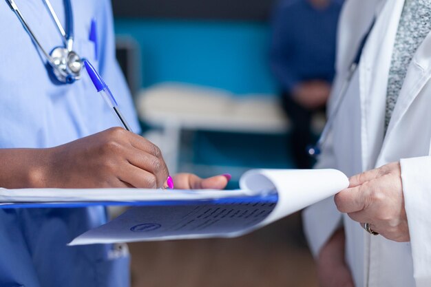 Крупным планом медсестра подписывает файлы с помощью врача в кабинете здравоохранения