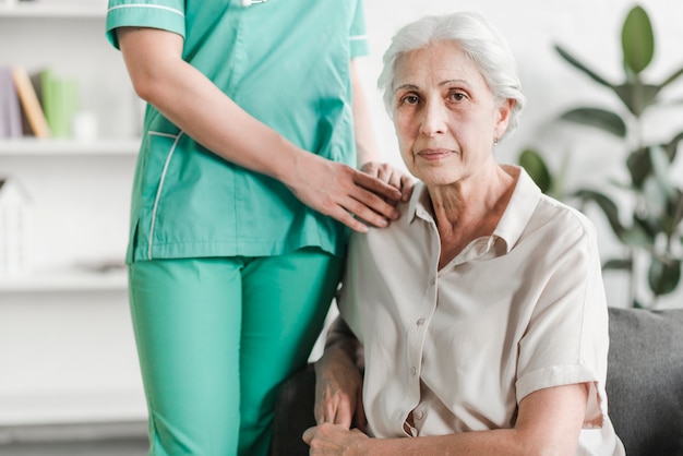 Close-up of nurse standing with senior female patient sitting on sofa