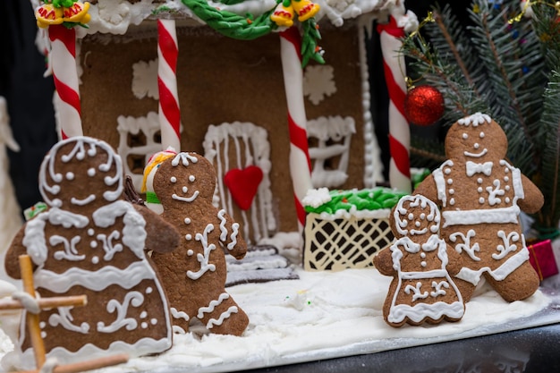 어두운 배경에 눈 덮인 집에서 만든 진저브레드 하우스 근처에 있는 귀여운 진저브레드 가족을 가까이서 보세요. 계절 제안 및 휴일 엽서 모형