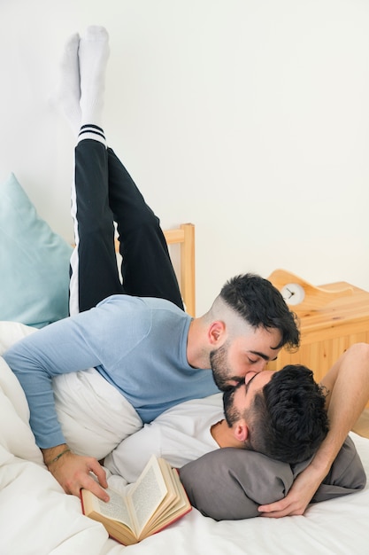 Бесплатное фото Крупный мужчина целует парня, лежащего на кровати с его ногой на стене