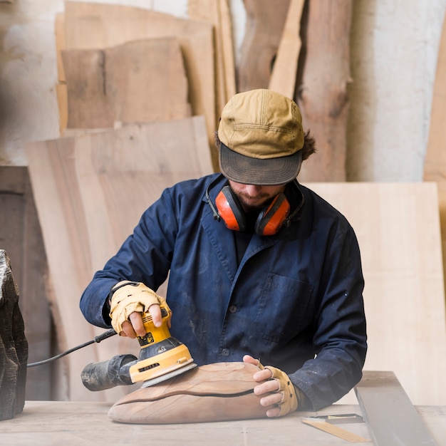Бесплатное фото Крупный план человека с ушным защитником на шее с помощью шлифовальной машины для разглаживания деревянных блоков