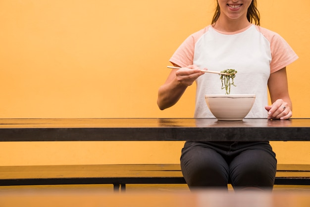 Бесплатное фото Крупным планом женщины едят зеленые водоросли с палочками на деревянный стол на желтом фоне