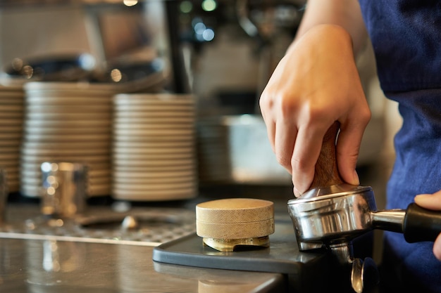 Бесплатное фото Крупный план женских рук бариста, нажимающих кофе на тампер, готовит заказ в кафе за прилавком
