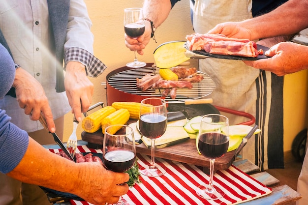 テーブルから食べ物やワインを取っている友人のグループのクローズアップ男性と女性が一緒に楽しんで休日を楽しんでいるバーベキュー屋外レジャー活動夏のお祝いの日 Premium写真