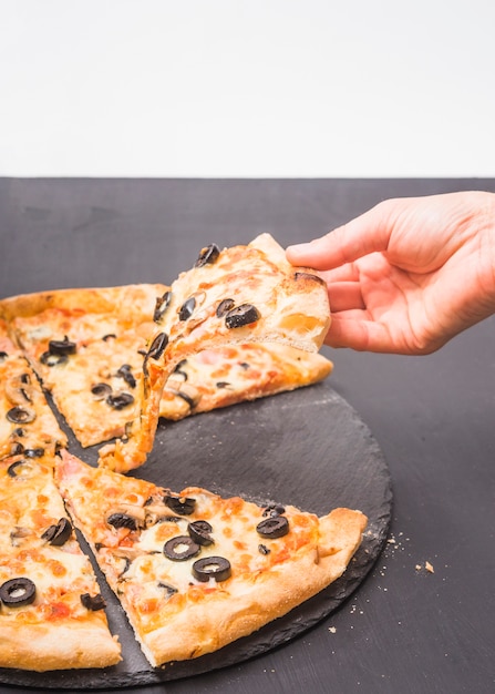 Бесплатное фото Крупным планом рука, проведение кусок пиццы на темном сланец