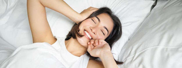 無料写真 枕の上でベッドに横たわり、笑顔で感じながら転がる幸せなアジアの女の子の接写