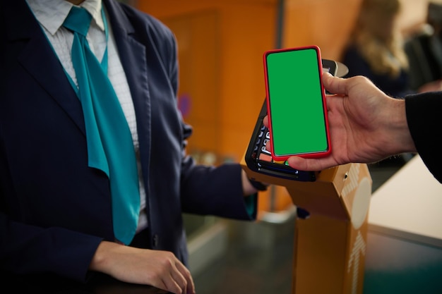 공항에서 항공편 체크인 보드를 통과하는 동안 은행 터미널 근처에서 모바일 앱 및 광고를 위한 복사 공간이 있는 녹색 크로마 키 빈 화면이 있는 휴대 전화를 들고 있는 남자의 손 클로즈업