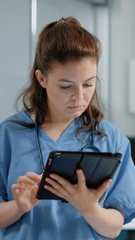 캐비닛의 의료 시스템에 대한 정보가 있는 태블릿 화면을 보고 있는 의료 보조원을 닫습니다. 연습을 위해 터치 스크린이 있는 가제트를 사용하는 간호사 전문가의 초상화.
