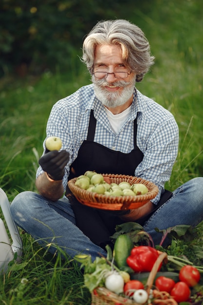 無料写真 野菜のバスケットを持って古い農家のクローズアップ。その男は庭に立っています。黒いエプロンのシニア。