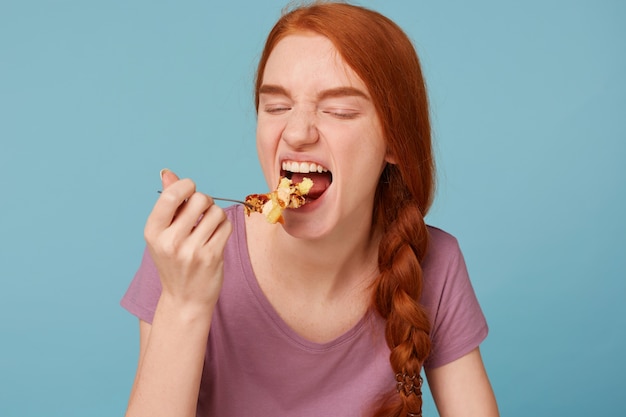 Крупным планом рыжая женщина с закрытыми глазами, протягивает ложку ко рту, ест калорийный торт