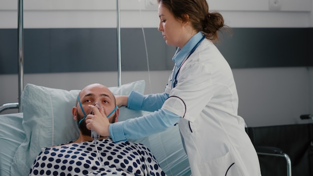 의사가 산소 마스크를 씌우는 동안 침대에서 쉬고 있는 아픈 남자 환자의 클로즈업