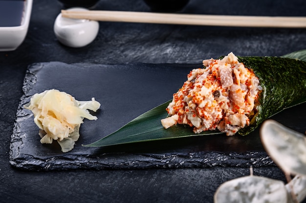 Крупный план вкусных суши-ролл с угрем и икрой тобико на темной каменной тарелке с соевым соусом и имбирем