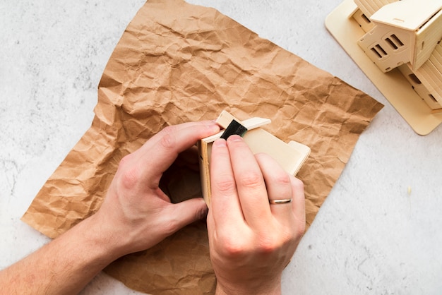 Бесплатное фото Крупный план женской руки, разглаживающей модель деревянного дома над коричневой мятой бумагой