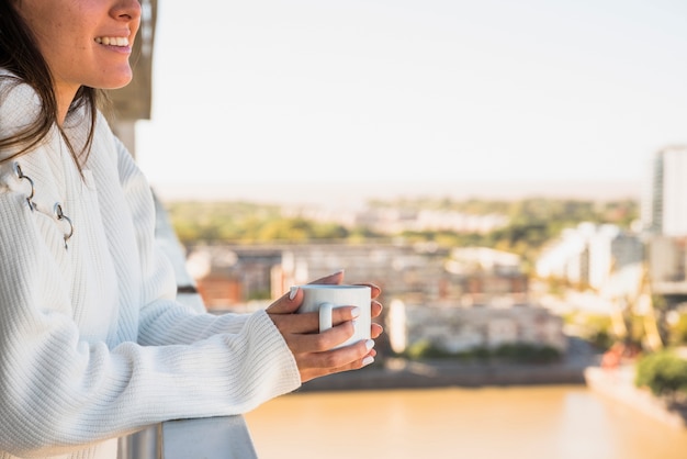 Бесплатное фото Крупный план женщины, стоящей на балконе с чашкой кофе